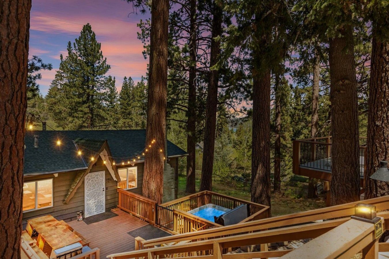 Une cabane dotée d’une terrasse, d’un bain à remous et d’un petit espace extérieur aménagé, le tout entouré de grands arbres.