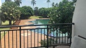 A pool area with palm trees, a wooden deck, and a white building.