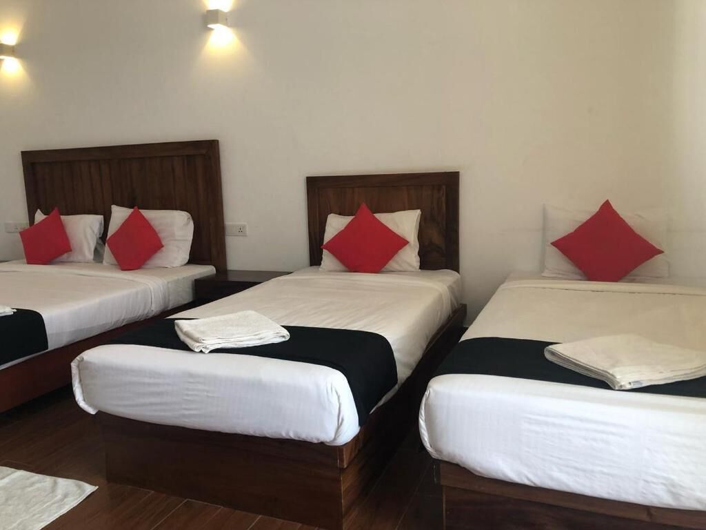 A hotel room with three single beds, each with a wooden headboard and white bedding.