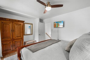 A bedroom with a bed, a ceiling fan, a wardrobe, a door, and a painting on the wall. - Kona Mansions#226 (Kailua-Kona)