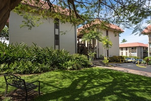 A building with a red-tiled roof, a grassy lawn, and a bench. - Kona Mansions#226 (Kailua-Kona)