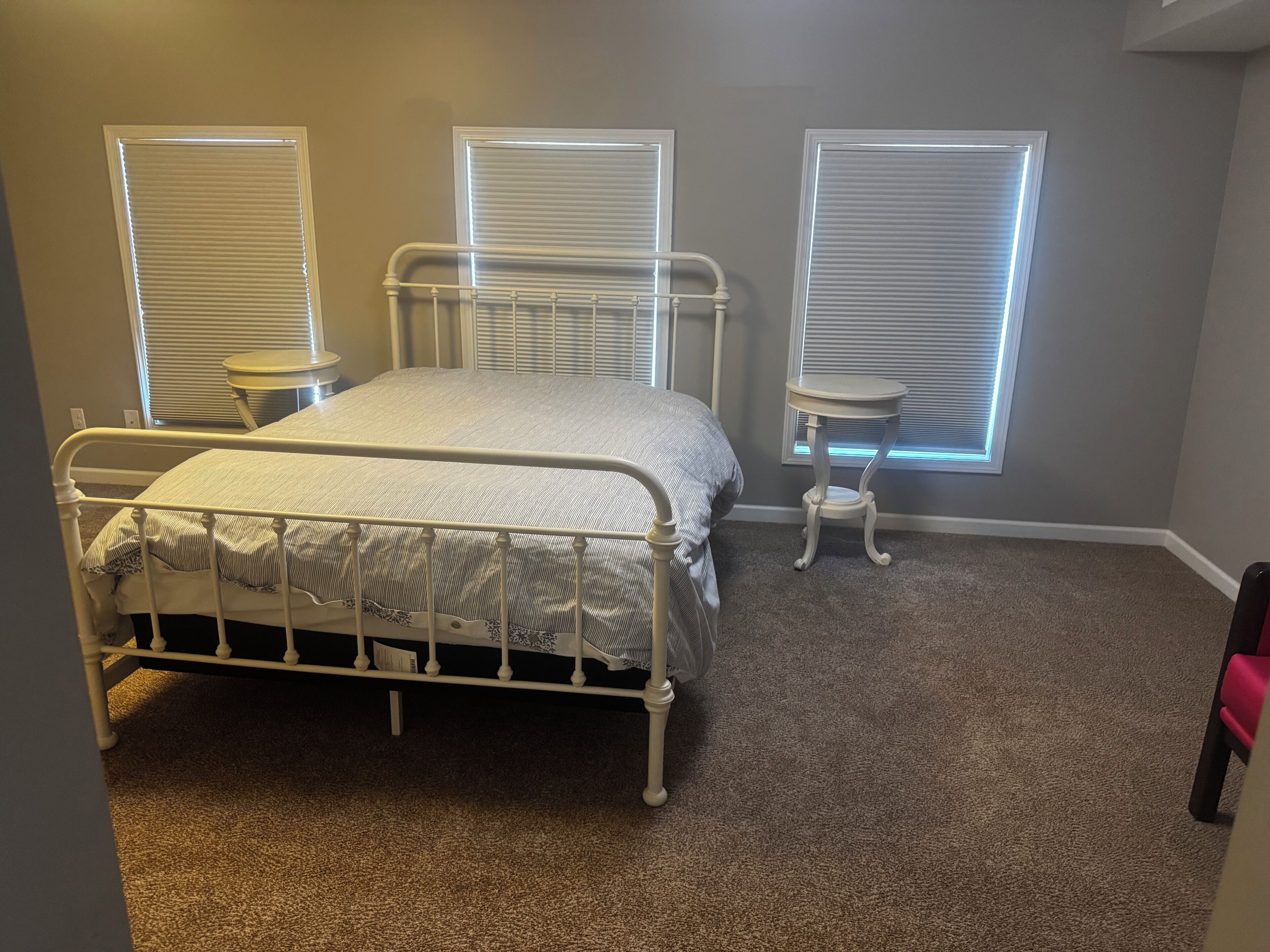A bedroom with a bed, two bedside tables, and three windows with blinds.