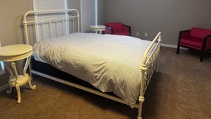 Une chambre à coucher avec un lit, une petite table ronde, deux chaises et une fenêtre avec des stores.