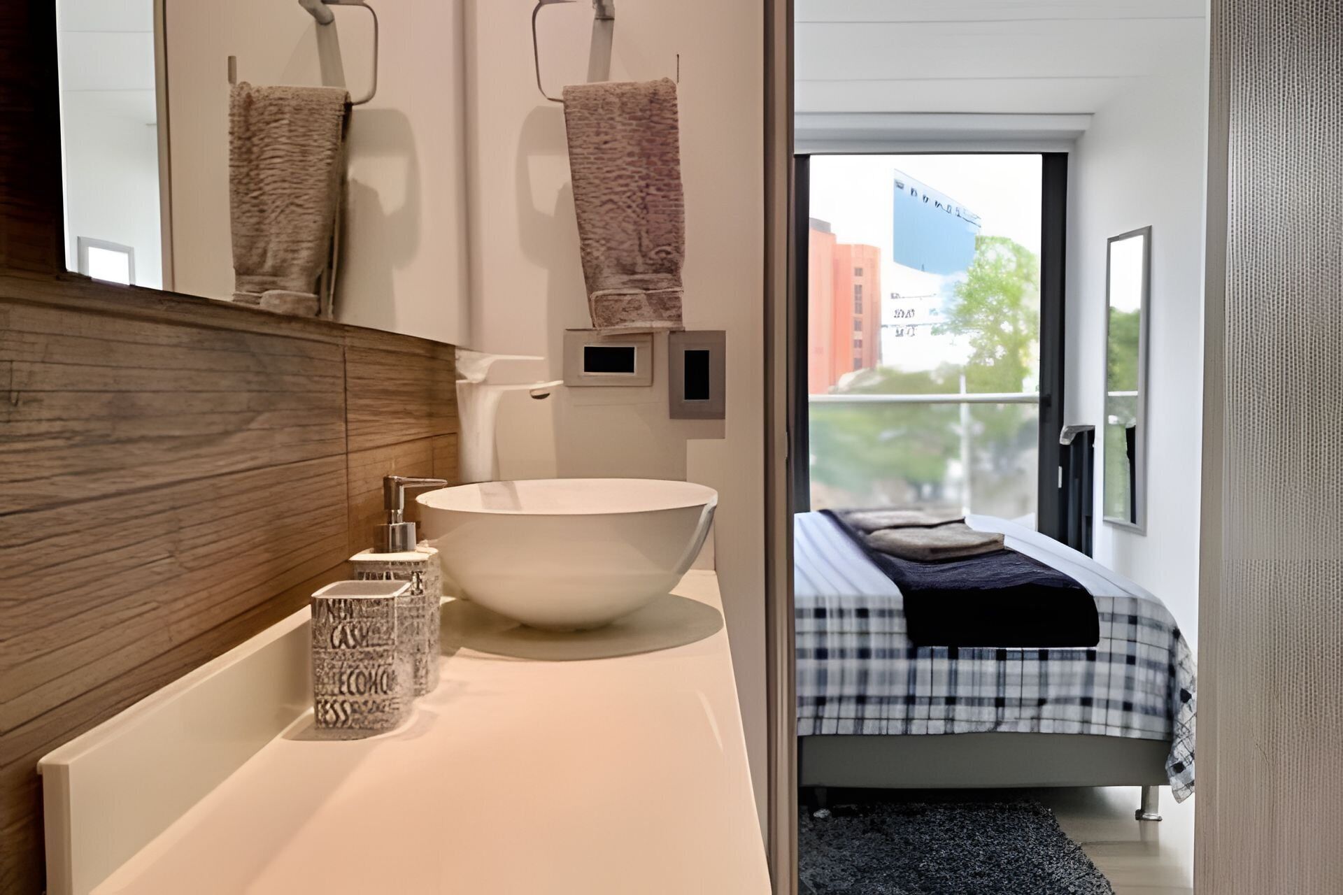 Un baño moderno con un lavamanos grande de color blanco, un mueble de tocador de madera y un perchero para toallas.