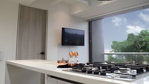 Moderni keittiö, jossa on litteänäyttöinen televisio, suuri ikkuna ja näkymä puita kohti.