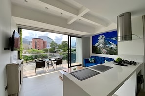 A modern kitchen with a large window, a dining area with chairs, and a blue sofa. - Apartamento en la zona más exclusiva de Pereira - by ALPES apartamentos (Pereira)