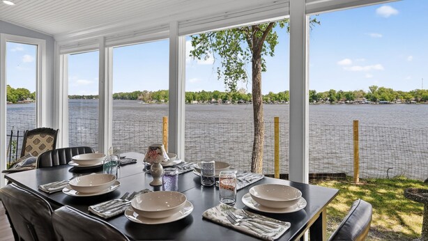 A dining area with a table set for four, large windows, and a view of a lake.