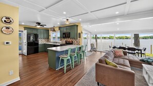 A spacious kitchen with a central island, green bar stools, and a view of a lake through large windows.