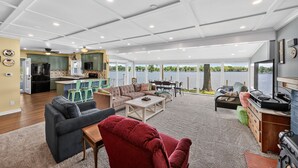 A spacious living area with a large window overlooking a body of water, a kitchen with green cabinets, and a dining area with outdoor seating.