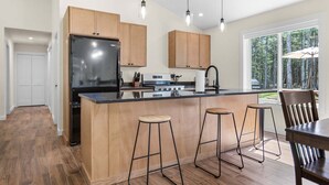 A modern kitchen with wooden cabinets, a black refrigerator, and a central island with stools. - Seal Point Escape - NEW! (Lamoine)