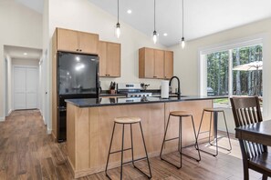 A modern kitchen with wooden cabinets, a black refrigerator, and a central island with stools. - Seal Point Escape - NEW! (Lamoine)