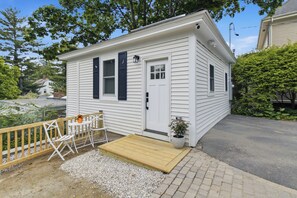 A small white house with a wooden deck, a door, and a window.
