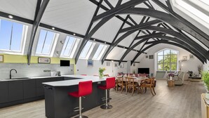 Eine moderne Küche mit Kochinsel, roten Barhocker und einem Essbereich mit Holztischen und -stühlen.