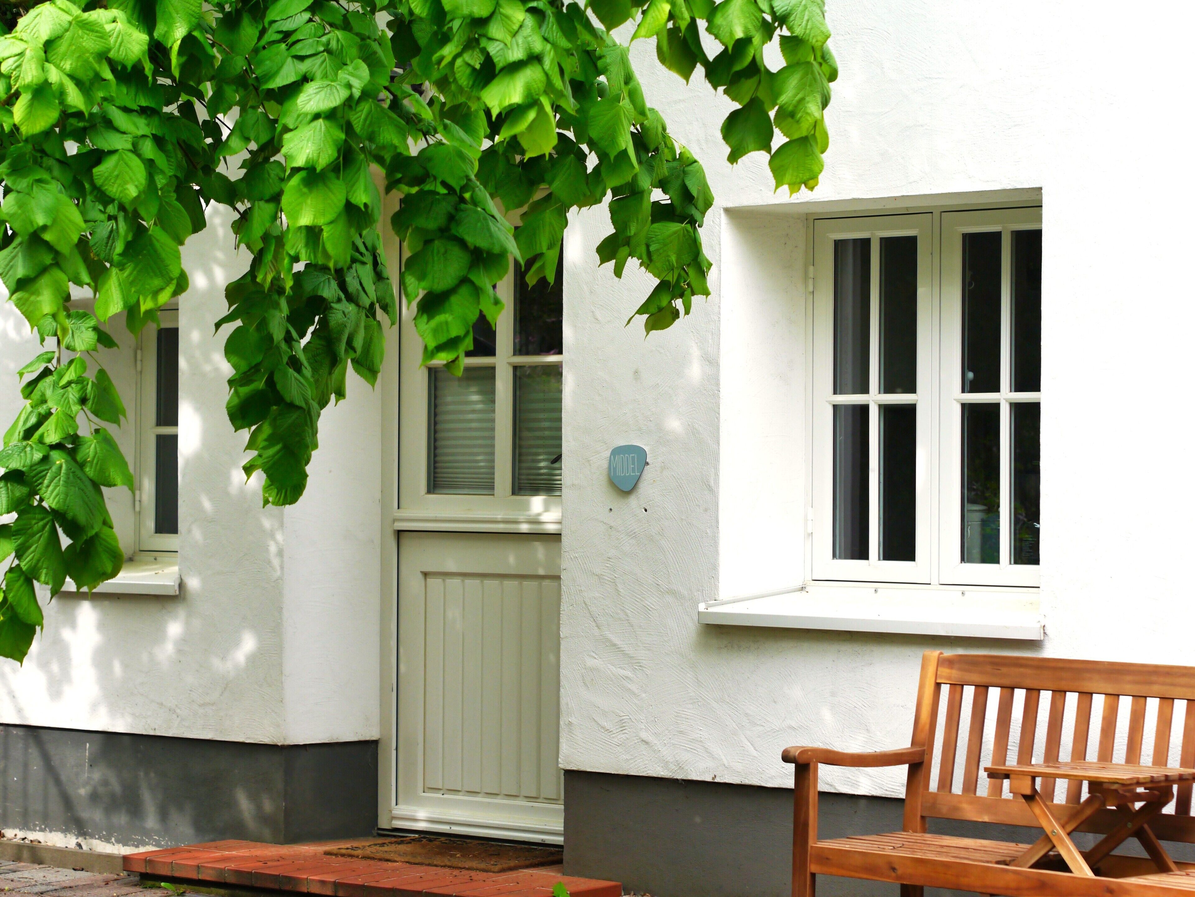 A white building with a wooden bench, a door, and a window.