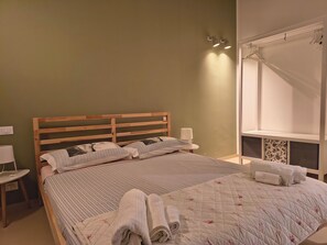 Ein ordentlich bezogenes Bett mit Kissen, ein Nachttisch mit Lampe und ein Fenster mit Vorhängen.