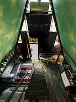 A narrow staircase with a metal railing, leading to a room with a green wall and a window.