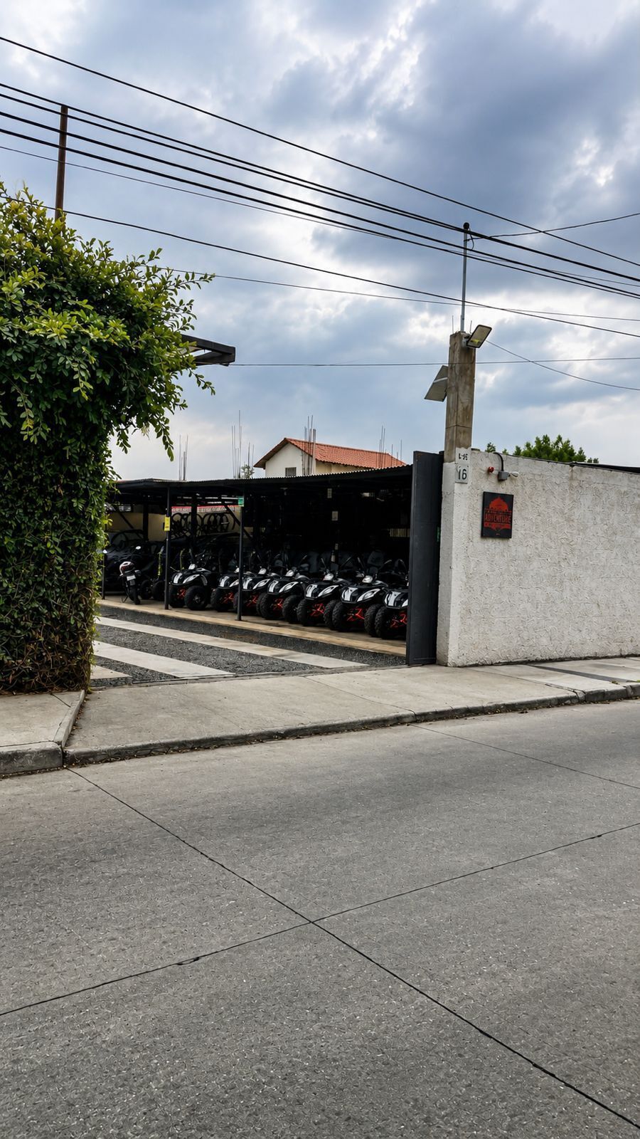 A parking area with several ATVs lined up, a concrete wall with a sign, and a building with a red roof in the background.