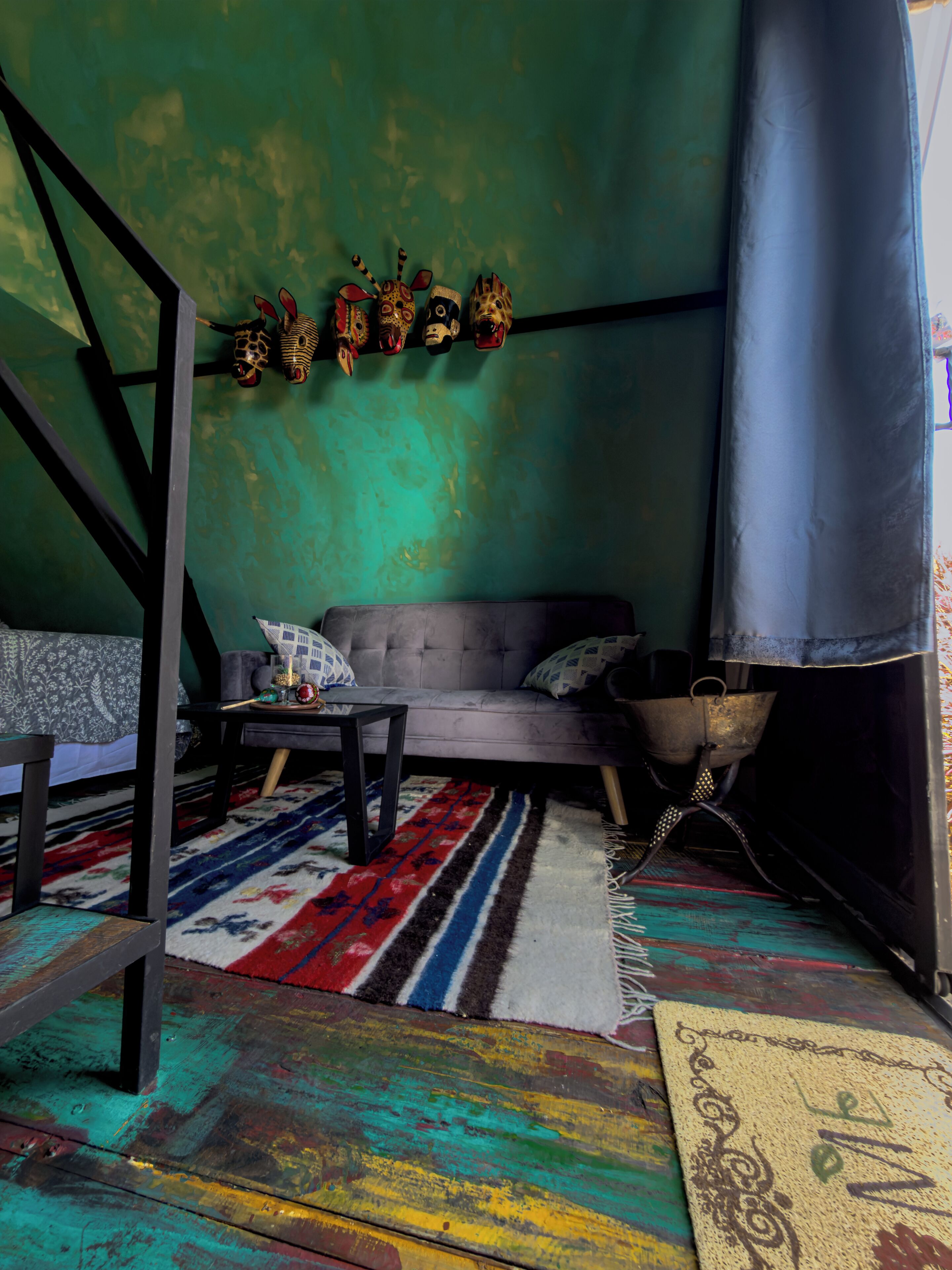 A room with a grey sofa, a patterned rug, a metal bucket, and a wall with decorative masks.