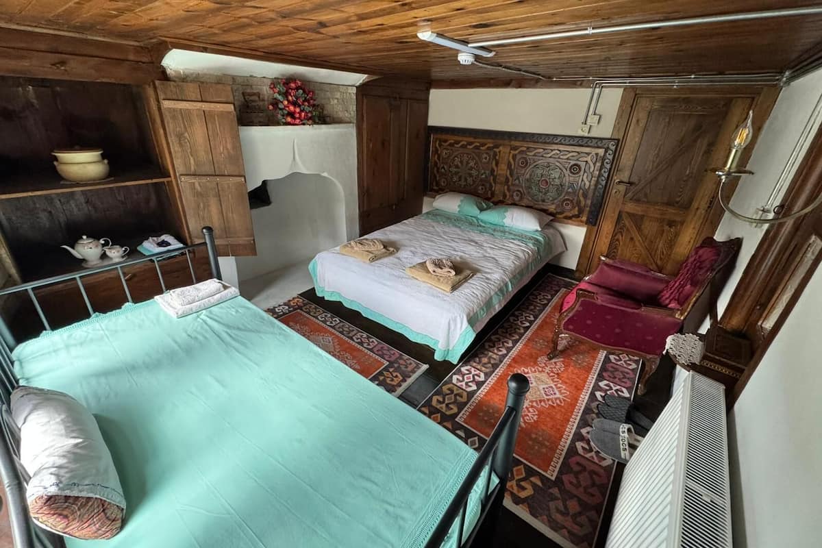 A room with a bed, a chair, a shelf with kitchenware, and a decorative headboard.