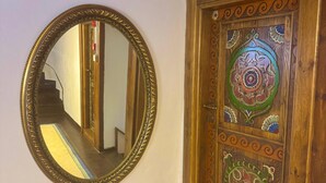 A room with a wooden ceiling, a round mirror on the wall, a wooden door with intricate designs, and a patterned carpet.