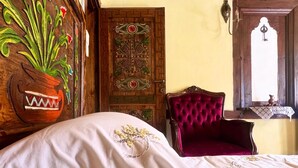 A room with a bed, a chair, a door with intricate designs, and a window with a view.