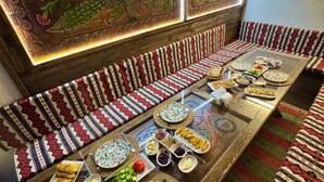 A traditional room with patterned cushions, a long table set with food, and decorative wall panels.