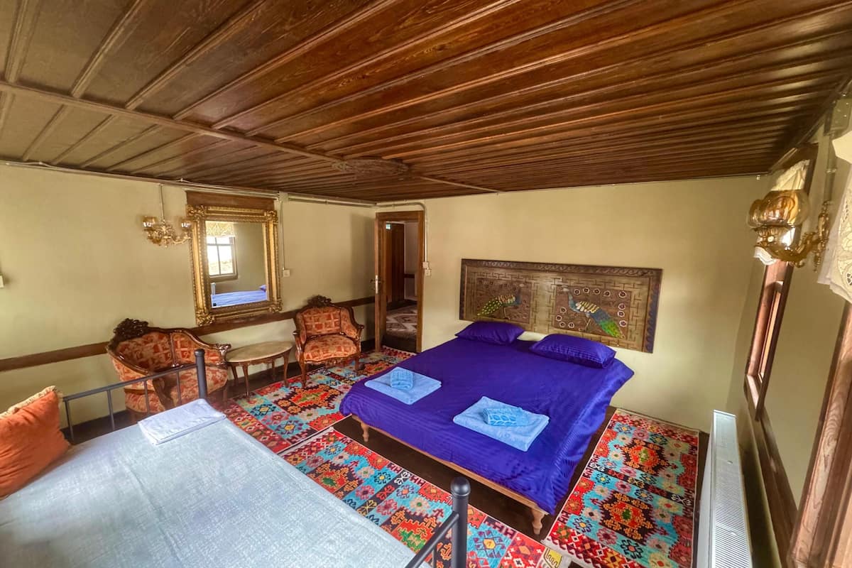A room with a wooden ceiling, a bed with a blue bedspread, a chair, a table, and a mirror.