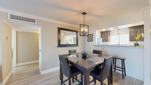 A dining area with a wooden table, chairs, a chandelier, and a kitchen area with cabinets and a window.