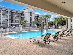 A hotel pool area with a clear view of the building in the background, a fenced pool, and lounge chairs. - Luxe 3BR Gulf View l Steps to Beach + Pool (Miramar Beach)