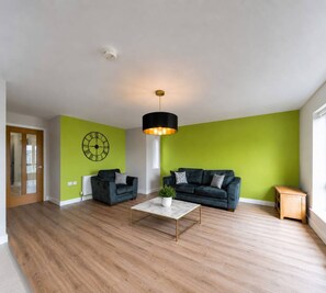 Una sala moderna con pared de acento verde, un sofá negro, una mesita de centro y una lámpara colgante negra.