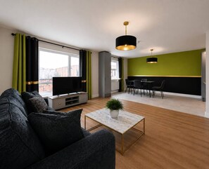 Ein modernes Wohnzimmer mit Sofa, Fernseher und Essbereich mit Stühlen.