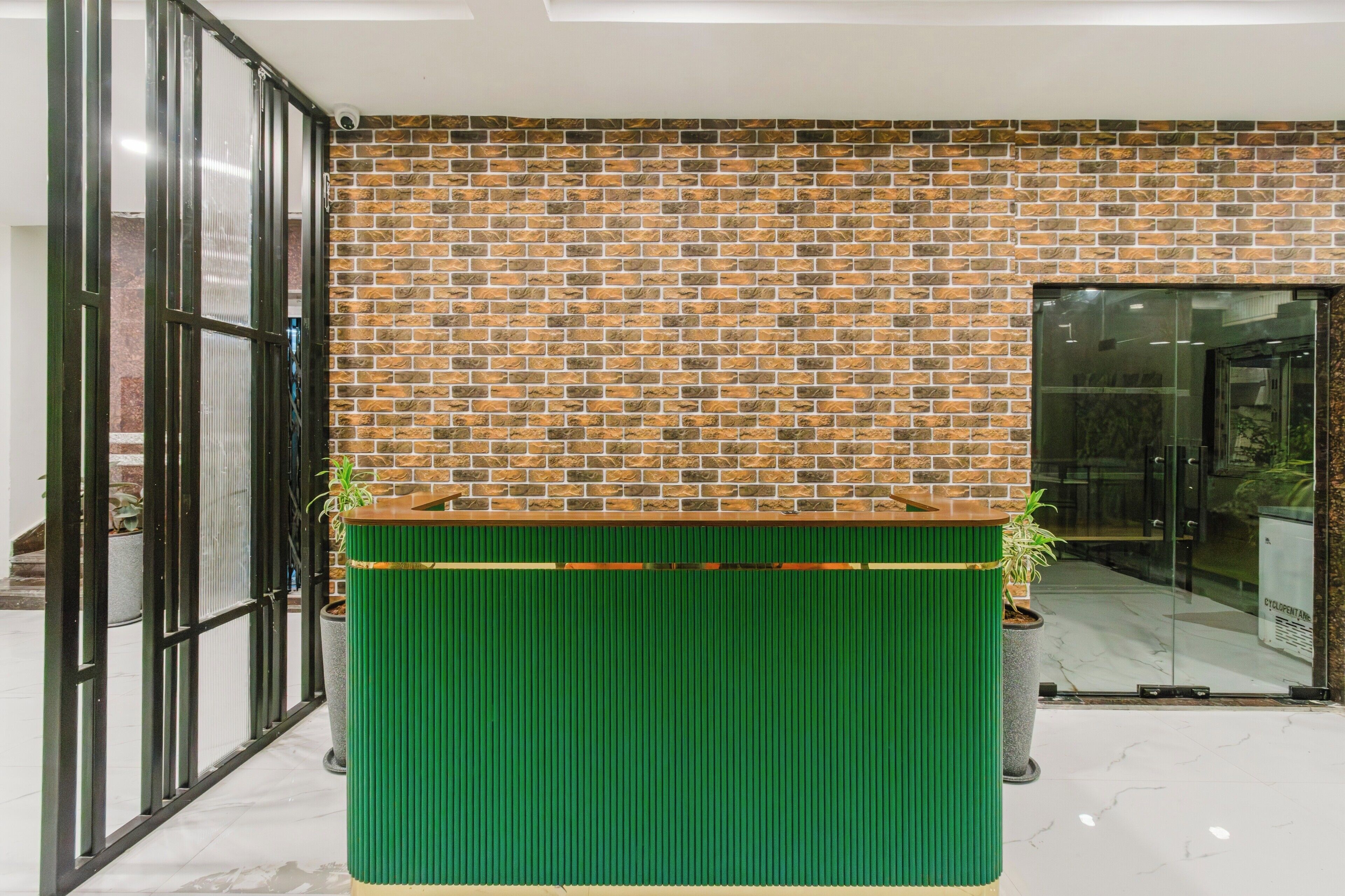 A reception desk with a brick wall backdrop, a glass door entrance, and potted plants.