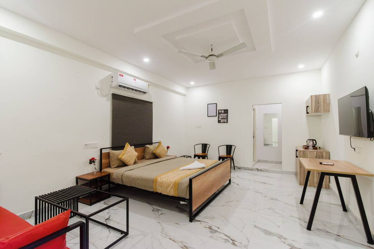 Quarto de hotel moderno com cama, escrivaninha, cadeira, televisão e ar condicionado.