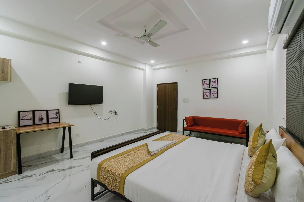 Quarto de hotel com cama, escrivaninha, televisão e ventoinha no teto.
