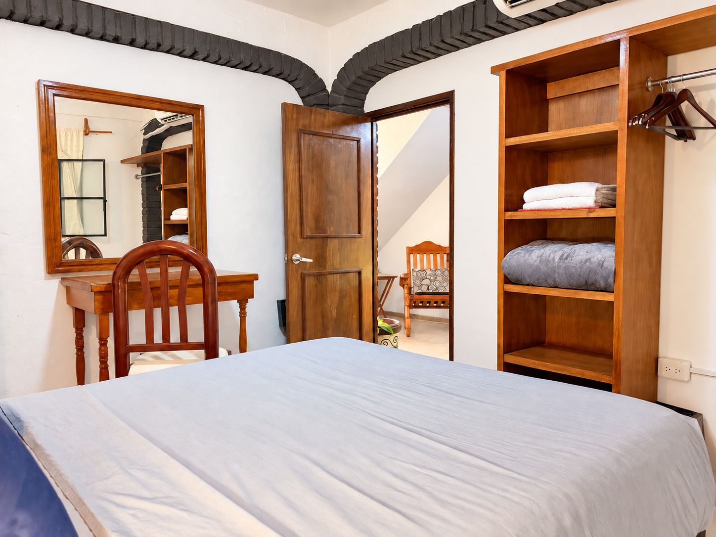 A bedroom with a bed, a wooden desk, a chair, a wardrobe, and a mirror.