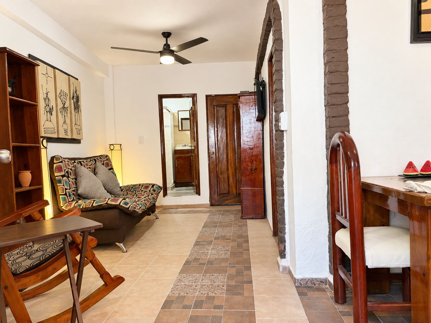 A cozy living area with a sofa, wooden furniture, a ceiling fan, and a tiled floor.