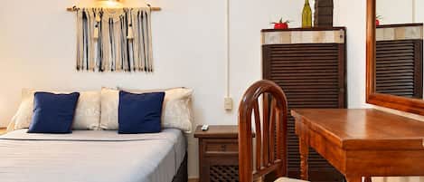 A bedroom with a bed, bedside table, chair, lamp, and a wall-mounted shelf with a bottle.