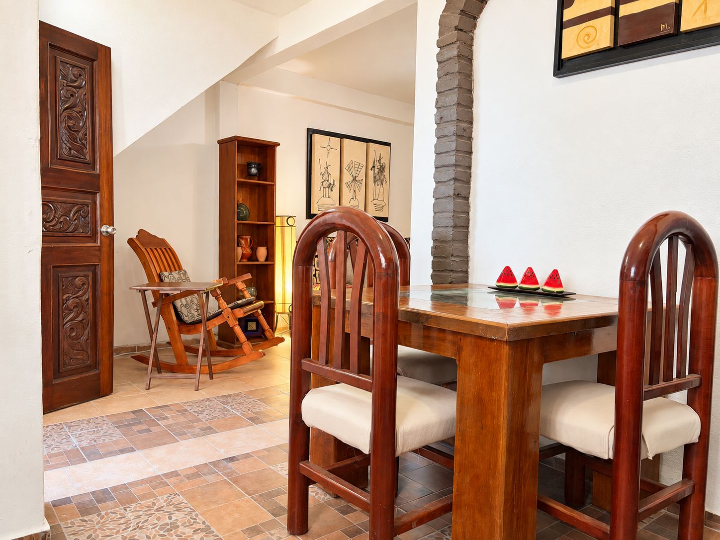 A dining area with a wooden table and chairs, a bookshelf, and a decorative wall piece.