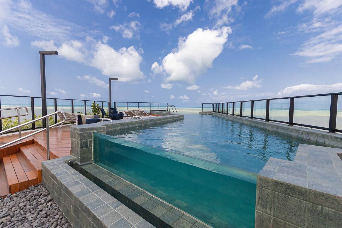 A swimming pool with a view of the ocean, surrounded by a deck and railings.