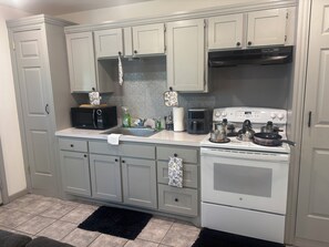 Una cocina con gabinetes grises, un microondas, una cafetera, una estufa y un lavaplatos.