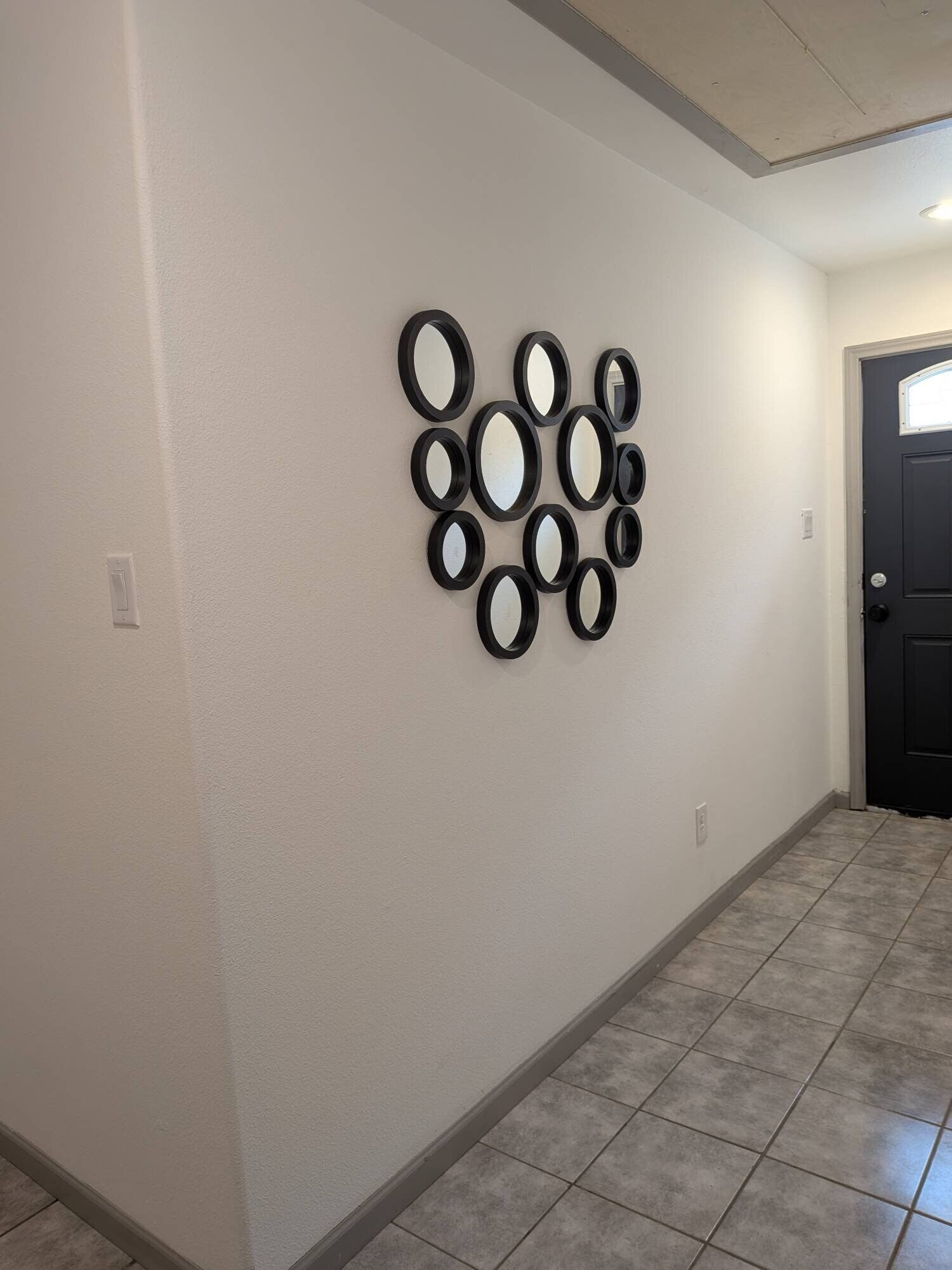 A hallway with a tiled floor and a wall-mounted mirror arrangement.