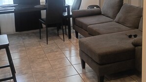 Een woonkamer met een bank, een eettafel met stoelen, een bijzettafeltje en een deur met raam.