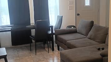 Ett vardagsrum med en soffa, ett matbord med stolar, ett litet bord och en dörr med ett fönster.