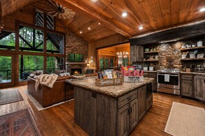 A rustic kitchen with a stone fireplace, wooden cabinets, and a large island with a 'S'mores Kit' sign. - Family Retreat on Fightingtown Creek • HotTub • FirePit • Games • Creek Access (Blue Ridge)
