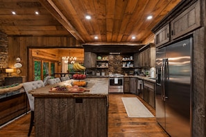 A spacious kitchen with wooden cabinetry, a central island with fruit, and a large refrigerator. - Family Retreat on Fightingtown Creek • HotTub • FirePit • Games • Creek Access (Blue Ridge)