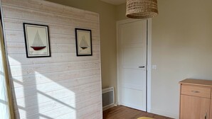 Een kamer met een houten vloer, een bed met een gele sprei, een witte deur en twee ingelijste foto's aan de muur.