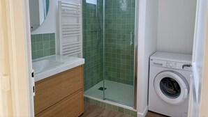 Een badkamer met een douche, een wasmachine en een houten wastafelmeubel.
