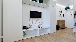 A room with a built-in TV, white shelving, and a wooden floor. - Reflet Azur - Modern Studio with Sea View Balcony (Fréjus)