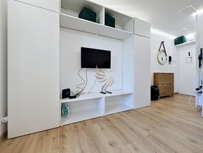 Una habitación con televisor integrado, estanterías blancas y piso de madera.