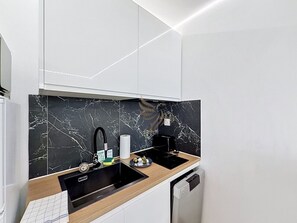 Eine moderne Küche mit schwarzem Marmor als Rückwand, einer Holz Arbeitsplatte, einem schwarzen Spülbecken und einem Geschirrspüler.